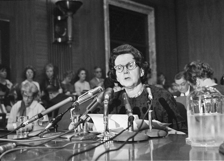 A woman speaks at table in front of several microphones during a congressional hearing.