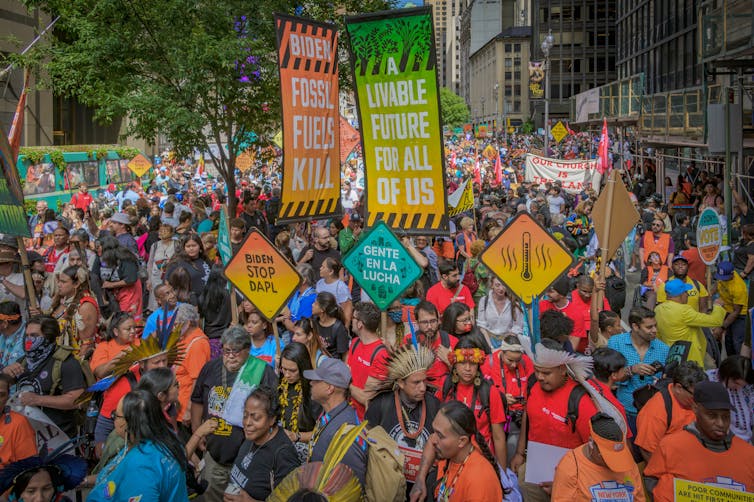 A street filled with people, many holding signs calling on the Biden administration to take action on climate change.