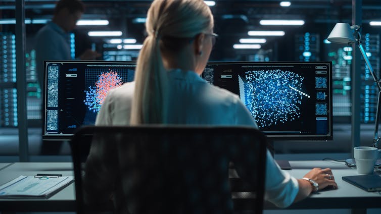 Female technical operator works with display showing neural network in the system control dark room